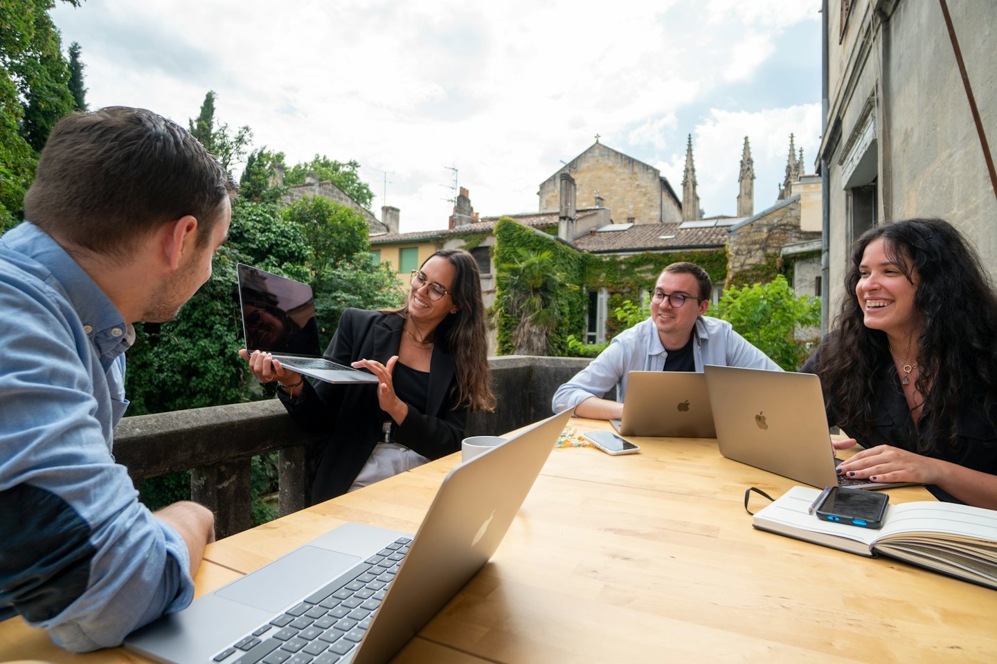 Czterech młodych profesjonalistów współpracuje przy stoliku na zewnątrz z laptopami.