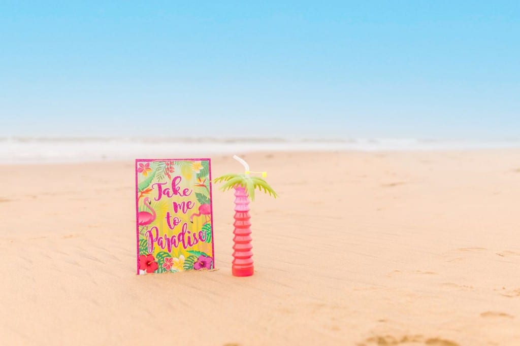 Kolorowy voucher i palmowy kubek na piasku plaży